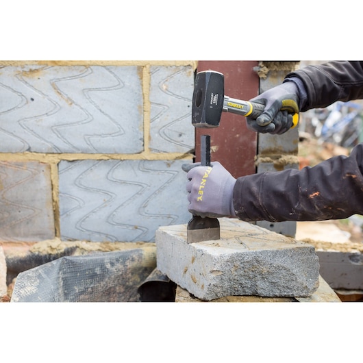 Photo of STANLEY STHT0-54128 sledge hammer in use, striking a chisel on a concrete block at a construction site.