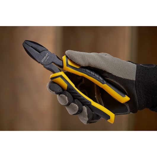 Photo of STANLEY STHT0-74454 combination pliers with yellow and black handles, held in a gloved hand.