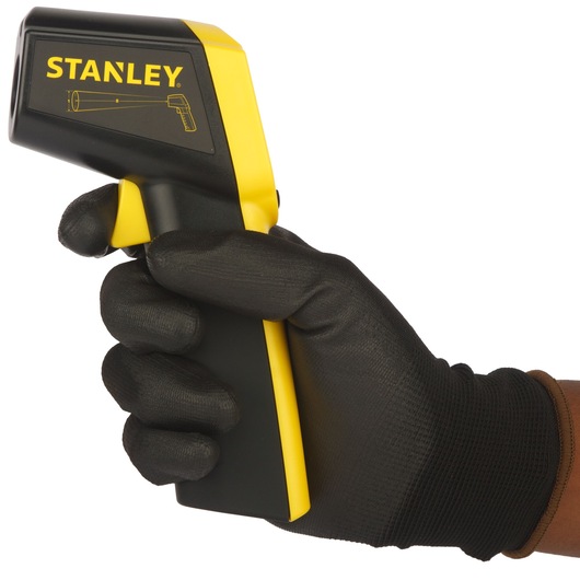 Photo of STANLEY STHT0-77365 infrared thermometer held in a gloved hand, black and yellow body, side angle.