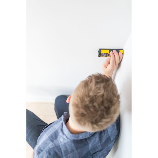 Photo of person using STANLEY STHT1-77032 stud sensor against a white wall, top-down angle.
