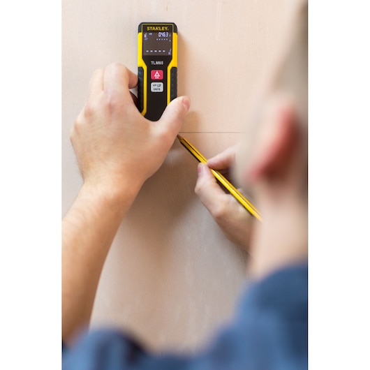 STANLEY STHT1-77032 laser distance measurer in use, person marking measurement on wood surface.