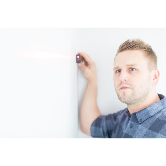STANLEY STHT1-77032 laser distance measurer held against a white wall in use, close-up photography.