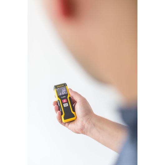 Photo of STANLEY STHT1-77032 laser distance measurer held in hand, display screen visible.