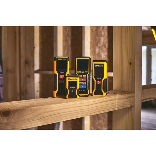 STANLEY STHT1-77032 digital laser distance meters displayed on wooden beam in construction setting.