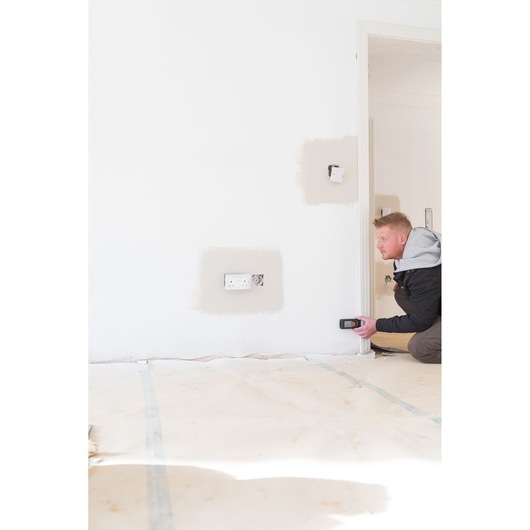 Photo of STANLEY STHT1-77142 wall scanner in use, person scanning white wall near electrical outlet.