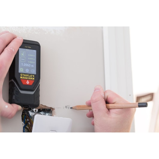 Stanley STHT1-77142 laser distance measurer in use, hand marking measurement on wall.