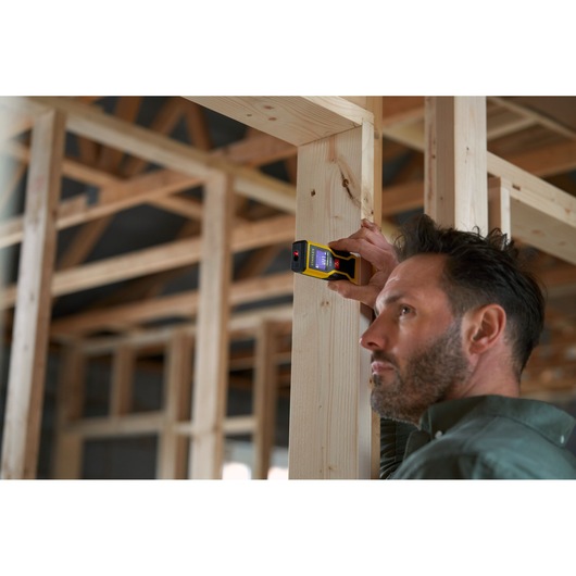 Photo of STANLEY STHT1-77409 digital laser measurer in use on wooden frame, construction site background.
