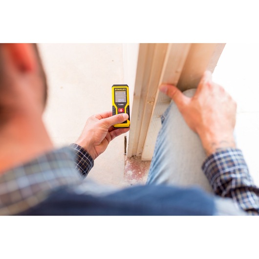 Photo of a person using a STANLEY STHT1-77409 laser distance measurer against a door frame.