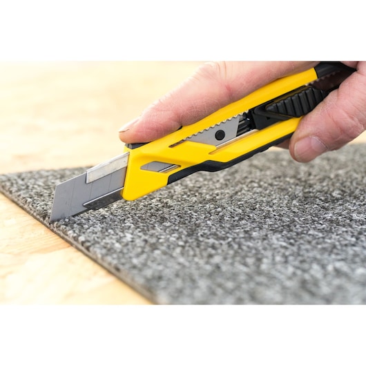 STANLEY STHT10266-0 utility knife with yellow and black handle cutting gray carpet close-up.