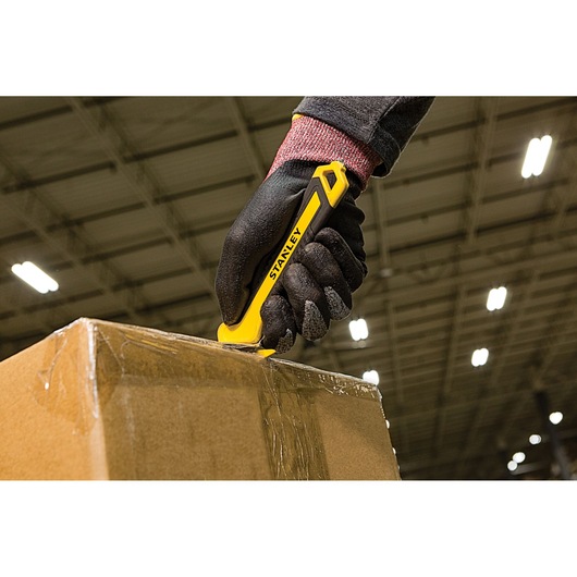 STANLEY STHT10356-0 utility knife cutting tape on a cardboard box in a warehouse setting.