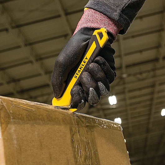 Stanley STHT10356 utility knife used to cut tape on a cardboard box, close-up, photo of product in use.