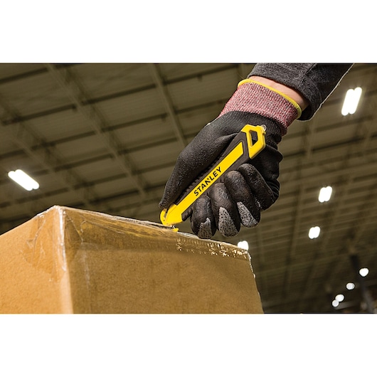 Stanley STHT10360-1 yellow utility knife used to cut cardboard box in warehouse setting.
