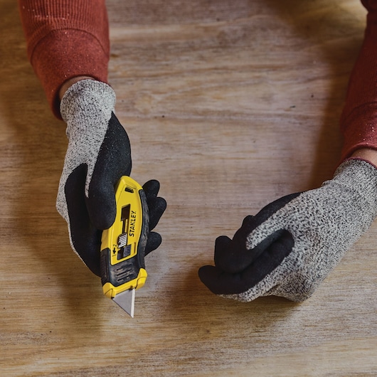 Photo of STANLEY STHT10432-0 utility knife held in gloved hand on wooden surface.