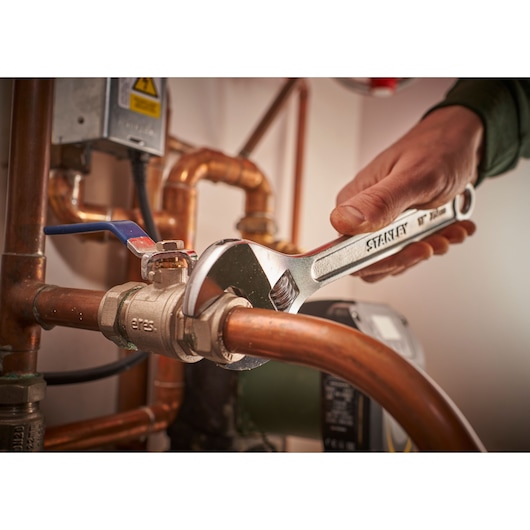Photo of STANLEY STHT13122-0 adjustable wrench tightening pipe fitting, plumbing context.