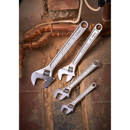 STANLEY STHT13123-0 adjustable wrenches set on dusty tiles near copper pipes, product photography.