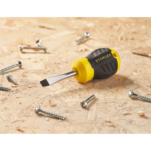 STANLEY STHT16147-0 stubby flathead screwdriver with yellow and black handle on wood with screws, angled view.