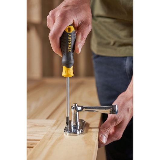 Photo of STANLEY STHT16163-0 screwdriver with yellow and black handle tightening hinge on wood.