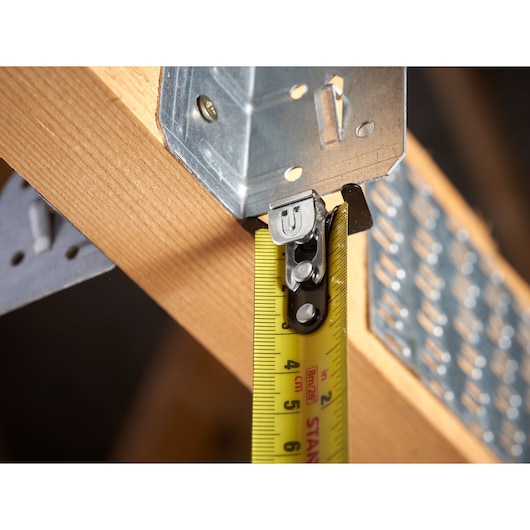 STANLEY STHT37236-5 tape measure close-up measuring wooden beam with metal bracket, yellow blade visible.