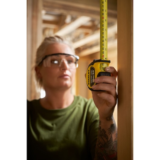 STANLEY STHT37237 tape measure held vertically against wooden beam in construction setting.