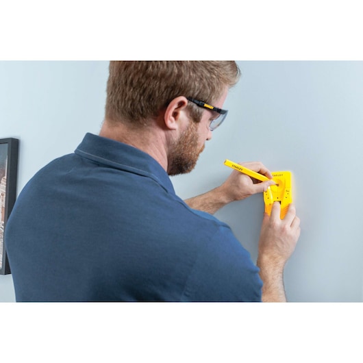 Photo of a person using a STANLEY STHT77587 yellow wall marking tool on a blue wall, photography category.