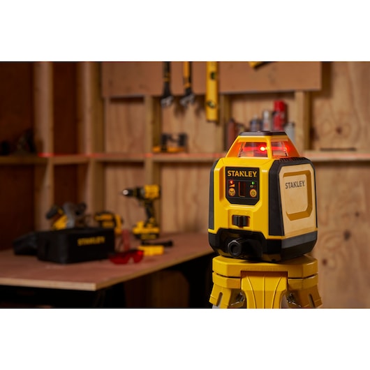 STANLEY STHT77616-0 laser level on tripod in a workshop with tools and workbench in background.