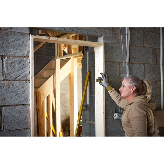 STANLEY STHT77666-0 laser distance measurer used by person on wooden door frame in construction site.