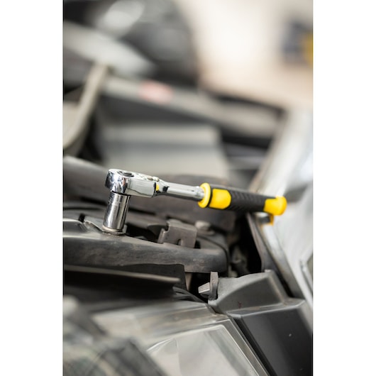 STANLEY STMT82663-0 ratchet wrench with yellow and black handle used on automotive part, side view.