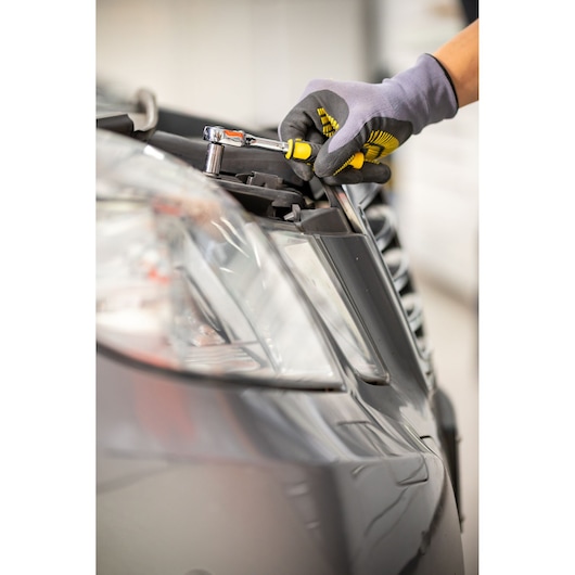STANLEY STMT82663-0 ratchet wrench used on car headlight, close-up with gloved hand.