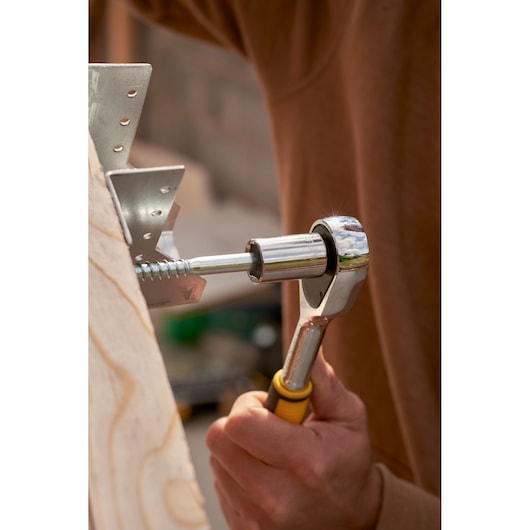 STANLEY STMT82831-1 ratchet in use tightening screw on metal bracket, close-up, yellow handle visible.