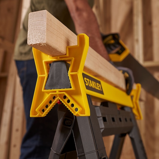 STANLEY STST1-70559 saw horse clamp holding wood beam, person sawing in workshop.