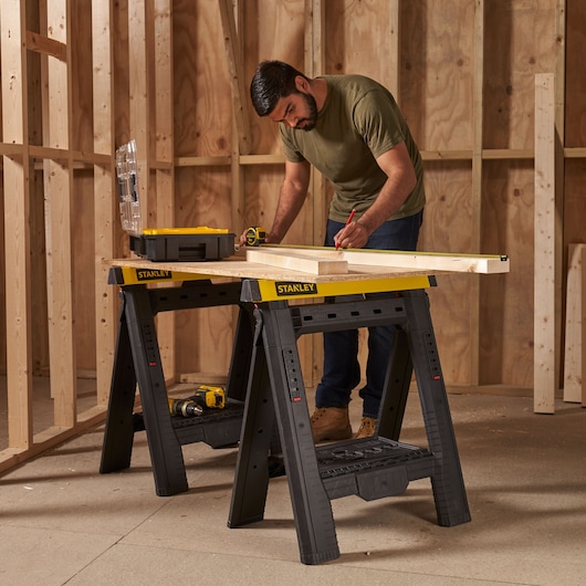 Stanley STST1-70559 plastic sawhorse pair with yellow tops supporting a work surface in a construction setting.