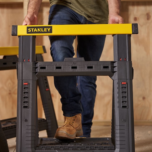 Photo of STANLEY STST1-70559 black and yellow sawhorse in use on a workshop floor.