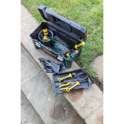 Photo of STANLEY STST1-75521 black toolbox with yellow-handled garden tools and gloves, shown outdoors.