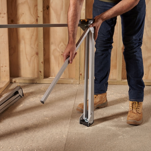 Photo of a person unfolding STANLEY STST81337-1 folding sawhorse in a workshop setting on a plywood floor.