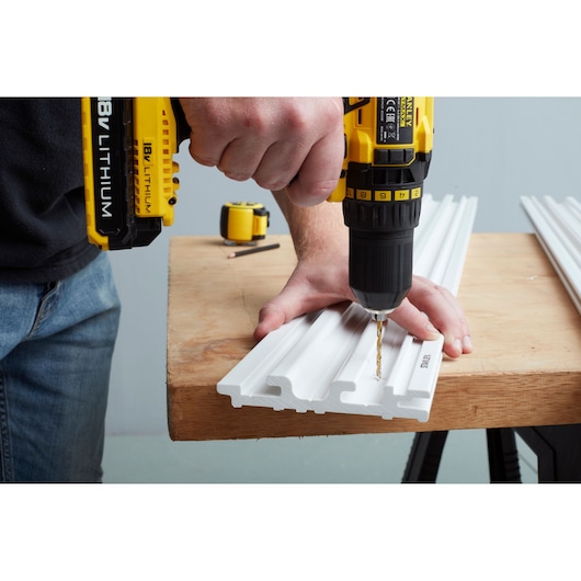 STANLEY STST82602-1 user drilling white plastic panel on workbench, close-up photography of product in use