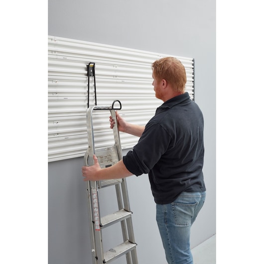 STANLEY STST82614-1 wall hook holding a metal ladder on a white slat wall, side angle photo.