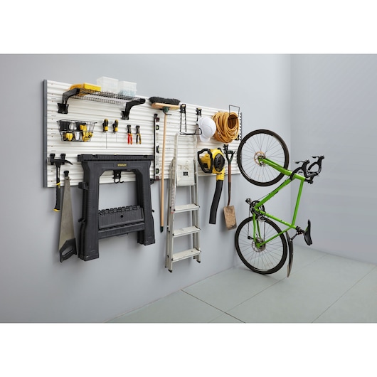 STANLEY STST82616-1 garage wall storage system with hooks, holding tools, ladder, workbench, leaf blower, and bicycle, angled view.