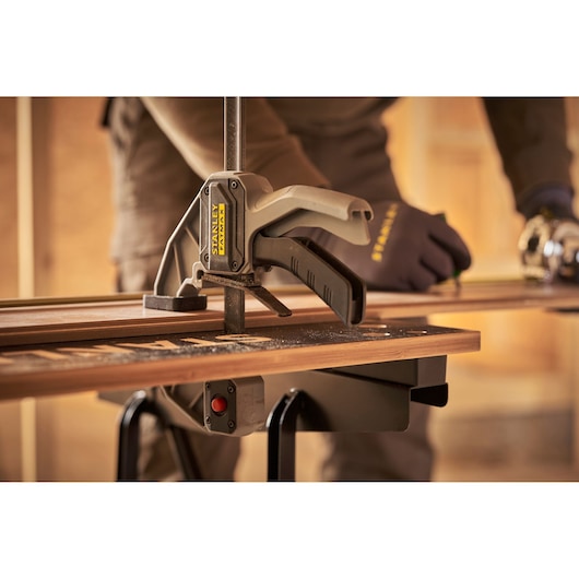Photo of STANLEY STST83400-1 clamp securing wood plank on workbench during woodworking project.