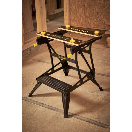 STANLEY STST83400-1 workbench with black metal frame, yellow accents, and adjustable clamps, shown in workshop.