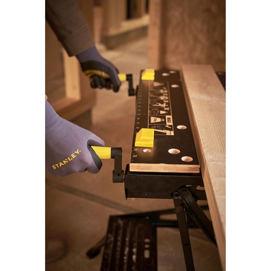 STANLEY STST83400-1 workbench with black top and yellow clamps, close-up of hands adjusting handles.