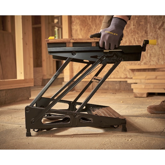 STANLEY STST83400-1 portable workbench with folding metal frame, shown in use on a construction site.