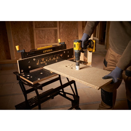 STANLEY STST83800-1 workbench holding wood while a person drills with a yellow power tool in workshop.