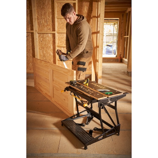 STANLEY STST83800-1 workbench shown in a workshop setting with tools on top and a person working nearby.
