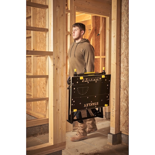 STANLEY STST83800-1 portable workstation folded, carried by person in a construction site setting.
