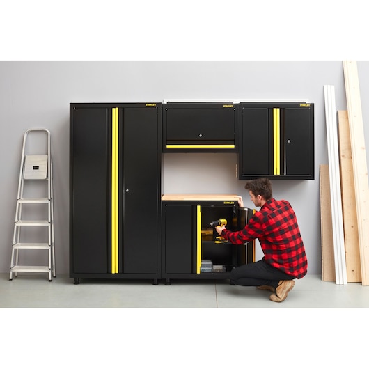 STANLEY STST97598-1 black and yellow garage storage cabinets, side angle, with person organizing tools.