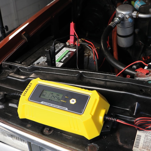 STANLEY SXAE00026GB electronic battery charger on car battery, close-up angle showing LCD screen and yellow casing.