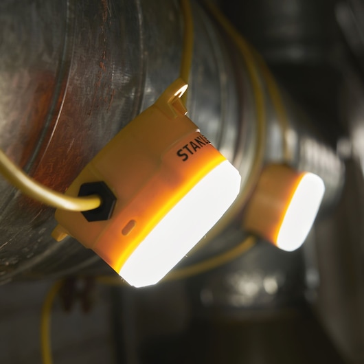 STANLEY SXLS31362E work light with yellow housing mounted on pipe, photo of illuminated portable light.