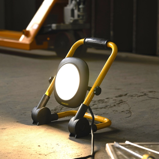 STANLEY SXLS35526E portable LED work light with yellow frame, illuminated on workshop floor.