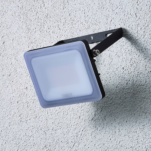 STANLEY SXLS38928E LED floodlight mounted on wall, angled view, black frame with frosted cover.