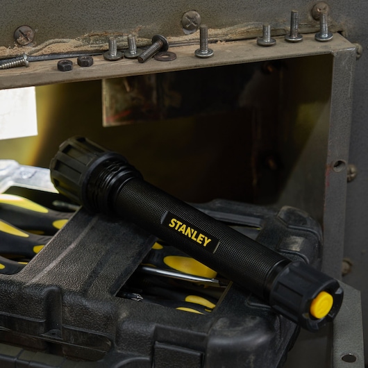 STANLEY SXLS50103E black flashlight with yellow button on tool case, indoor setting, side angle.